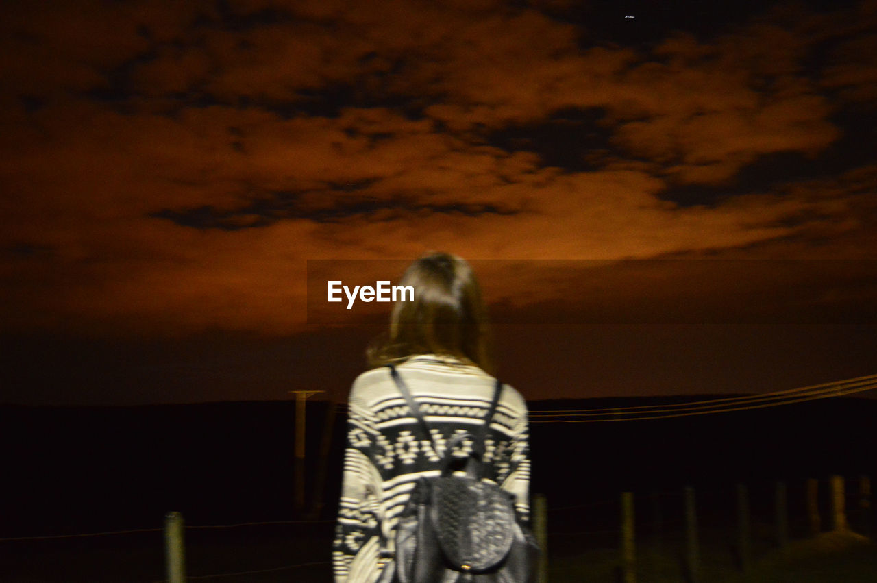 REAR VIEW OF WOMAN STANDING AGAINST SKY