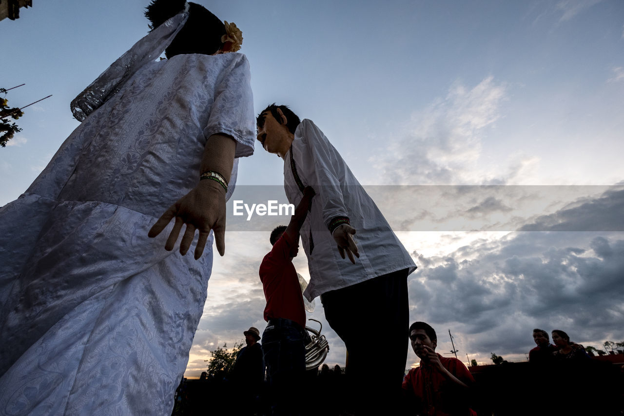 LOW ANGLE VIEW OF PEOPLE STANDING IN FRONT OF SKY