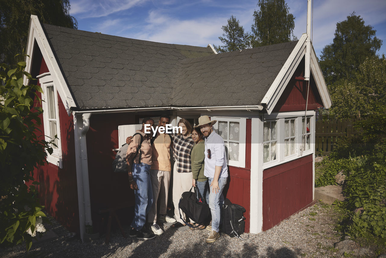 Smiling friends standing in front of wooden house