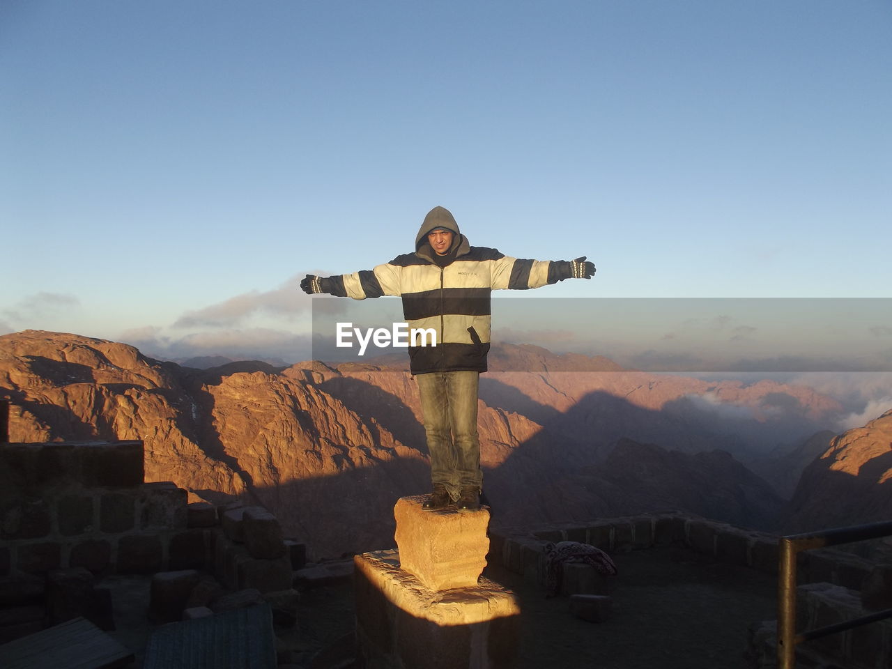 Full length of man with arms outstretched standing on rock against mountains and sky