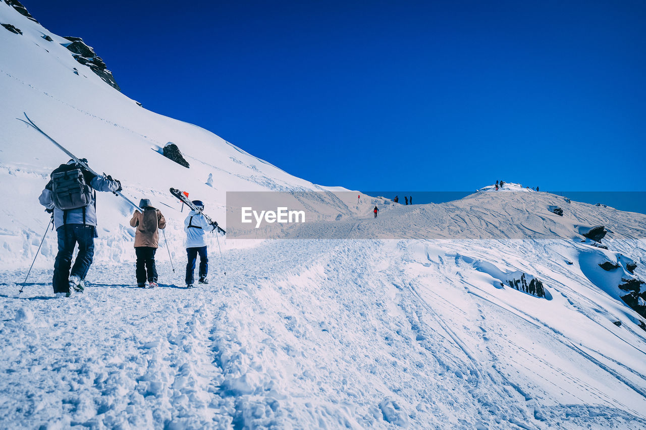 People on snowcapped mountain against clear blue sky