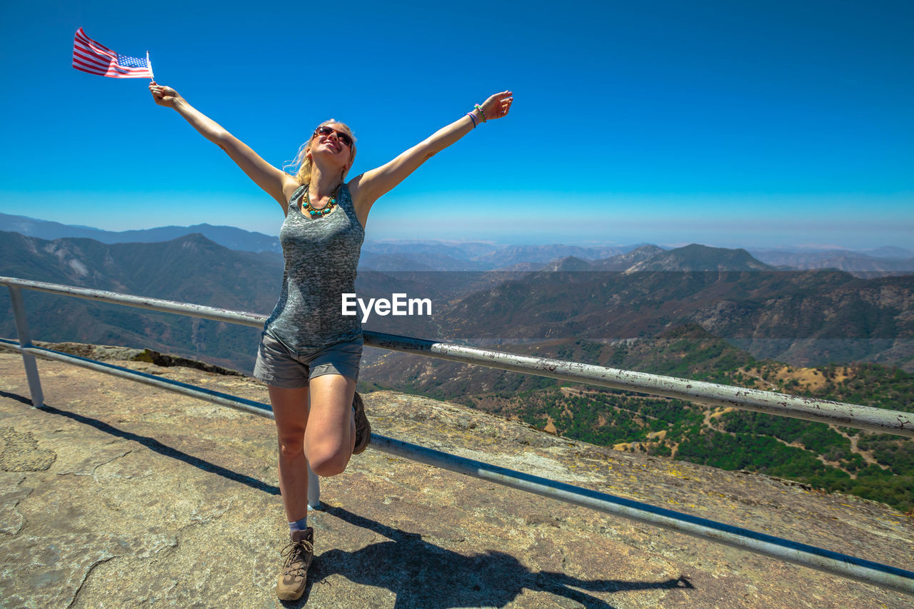 FULL LENGTH OF WOMAN WITH ARMS RAISED ON MOUNTAIN