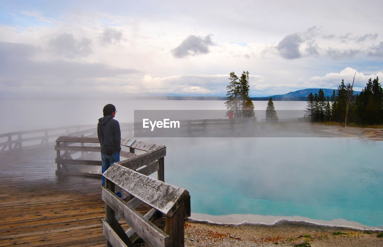 Rear view of man looking at lake against sky