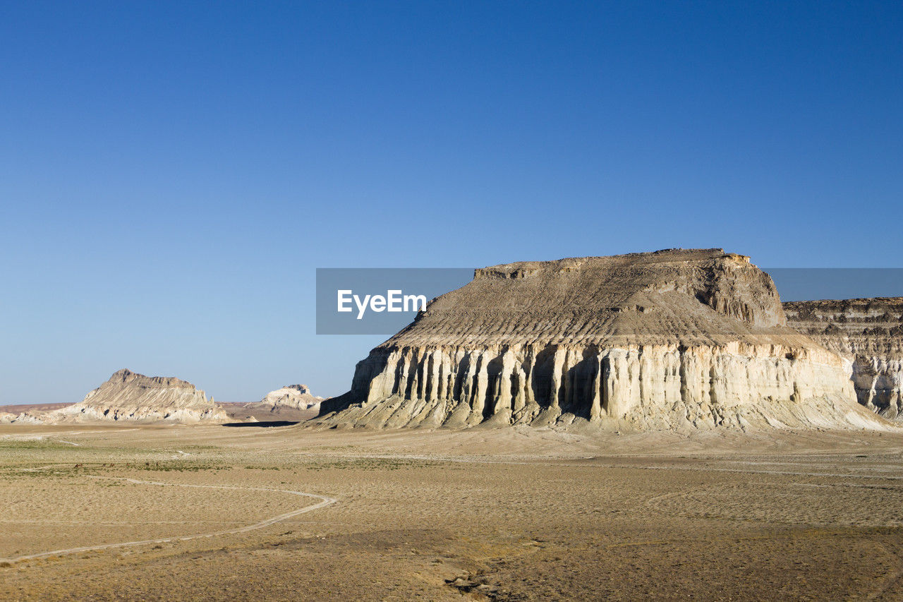 low angle view of rock formations on landscape against clear blue sky