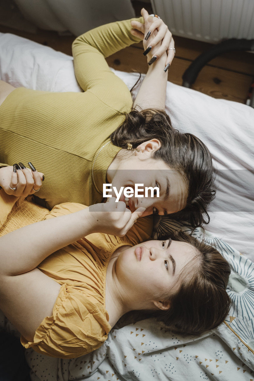 Directly above view of young woman with down syndrome touching nose of sister while lying down on bed at home