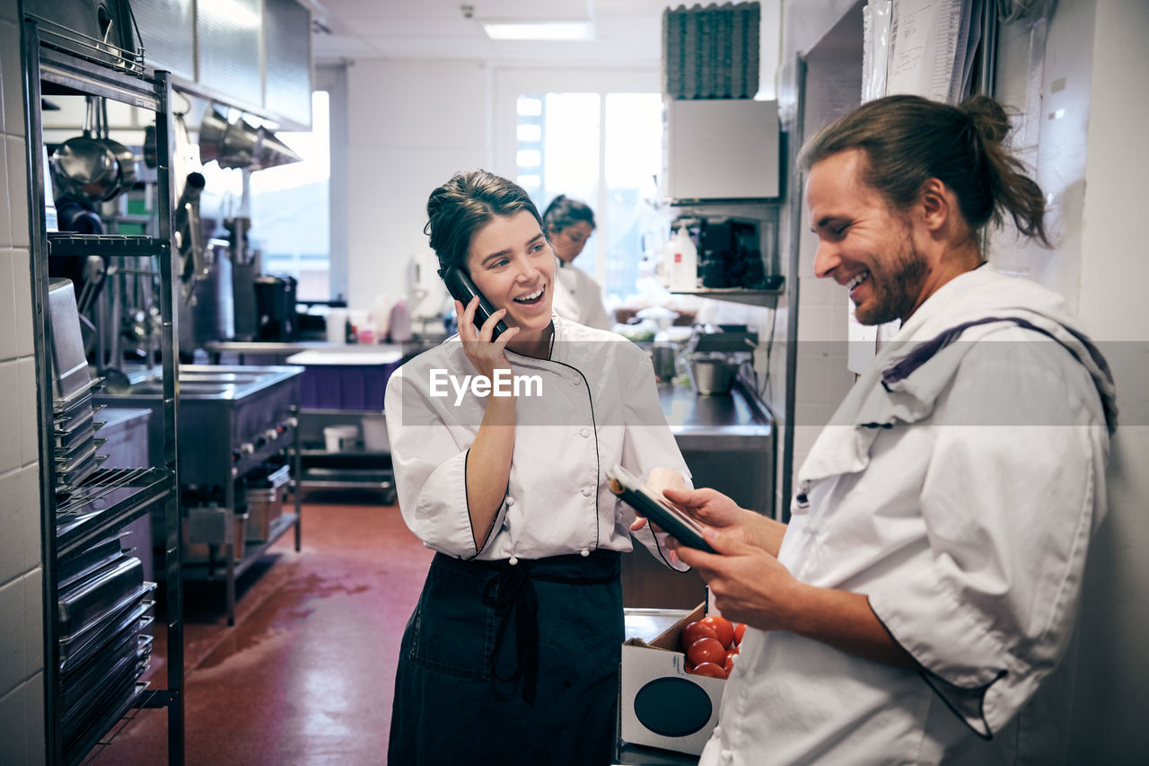 Male and female chefs using cordless phone and digital tablet in kitchen