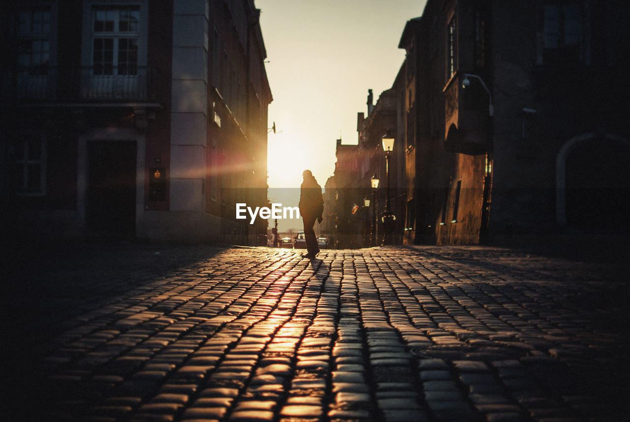 Silhouette man standing on cobblestone street in city