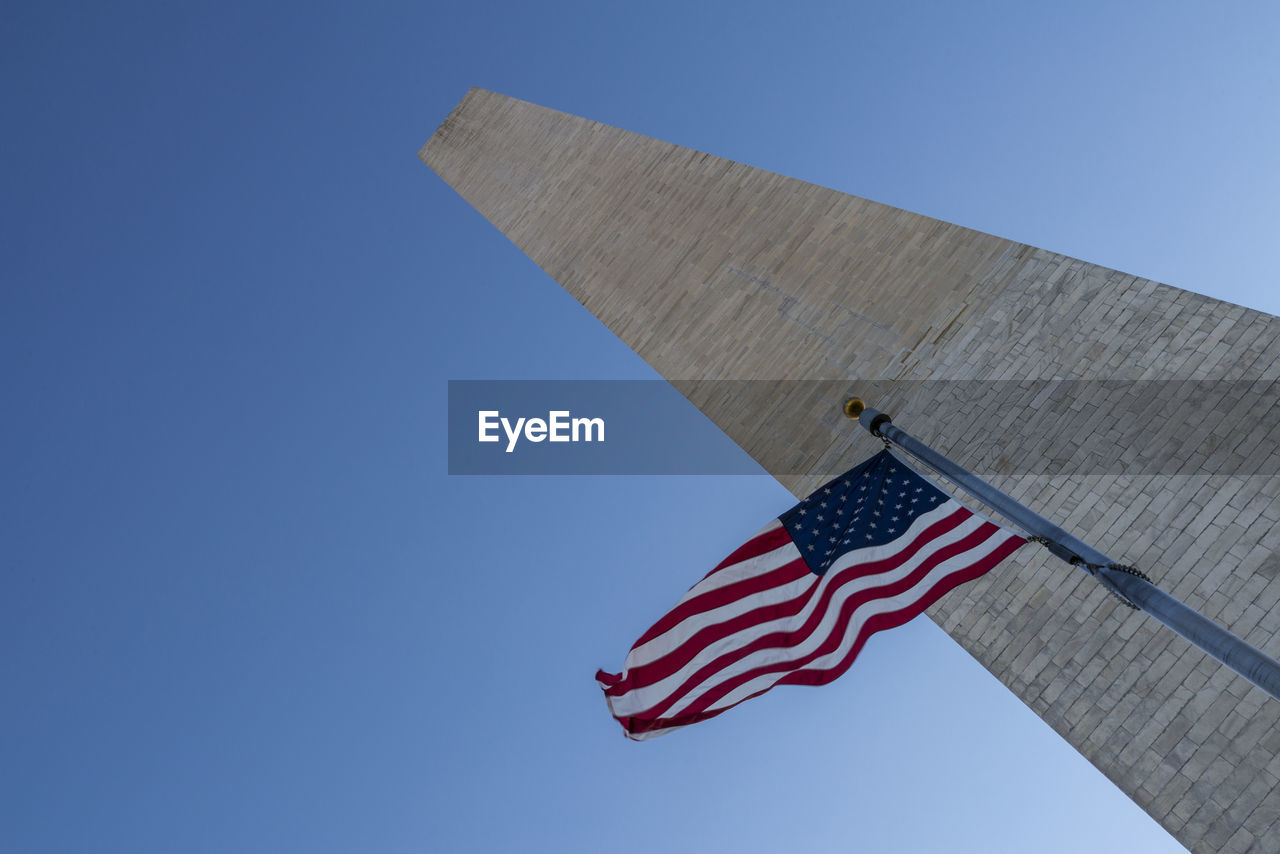 Low angle view of american flag and washington monument against clear blue sky