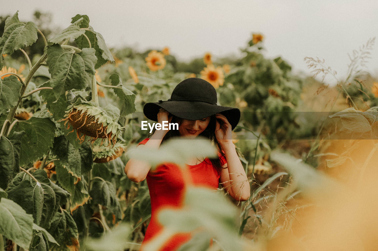 Woman standing amidst sunflower plants against sky