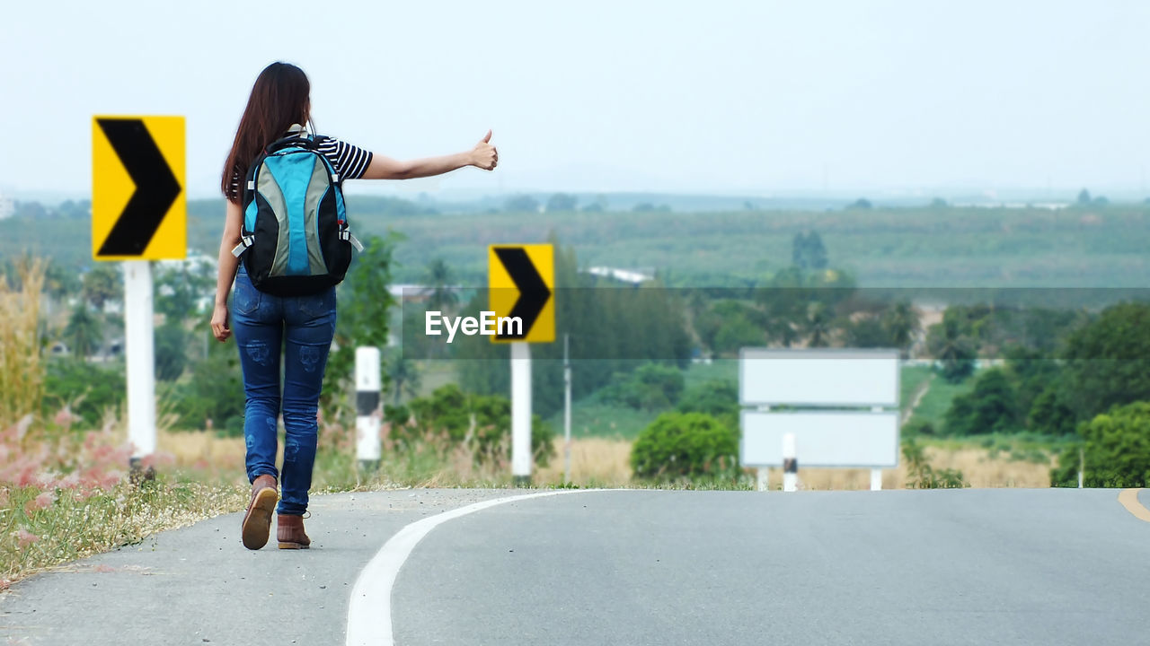Rear view of woman hitchhiking on road