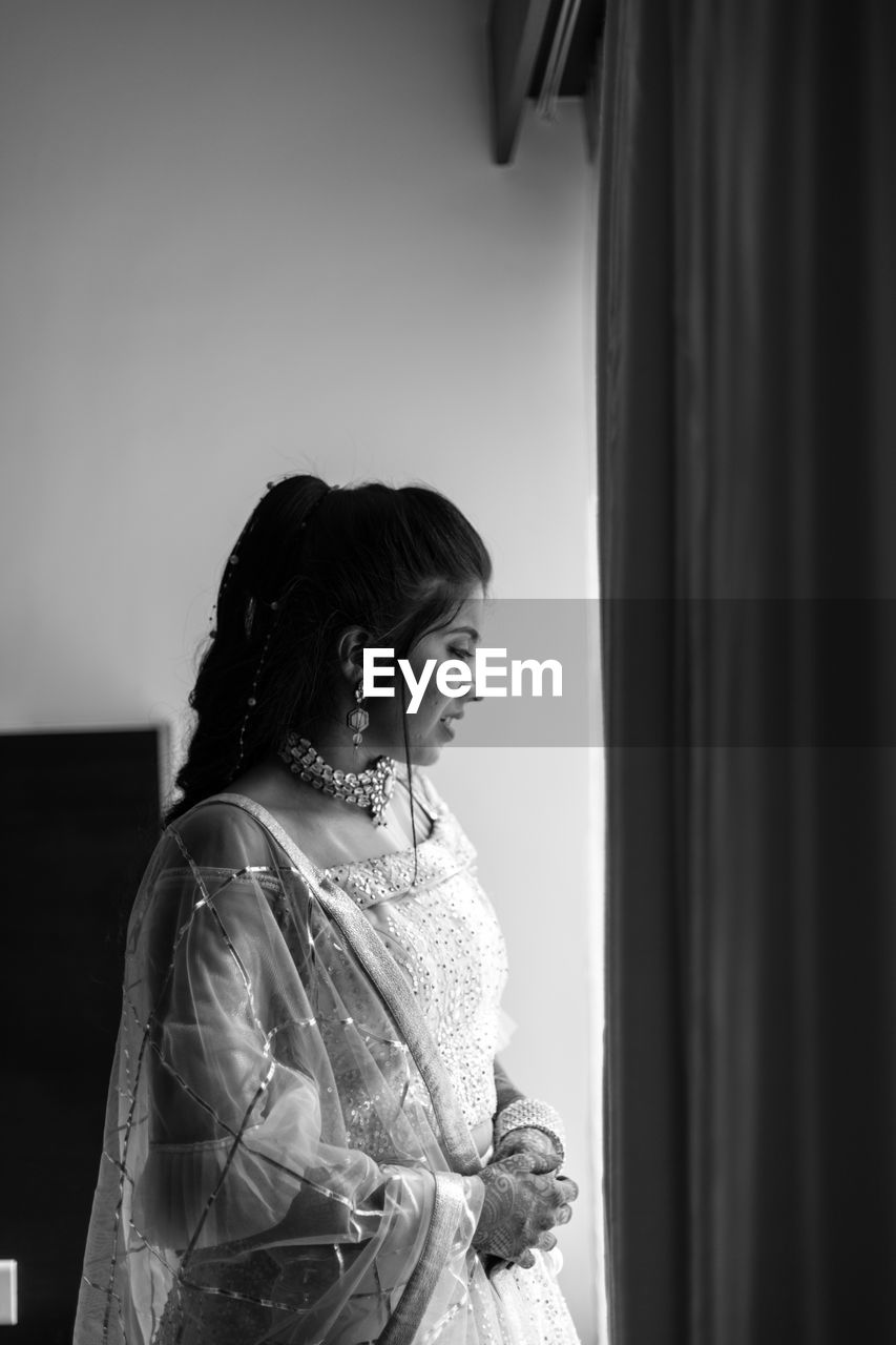 Black and white photography of woman looking thru the window  while standing at home