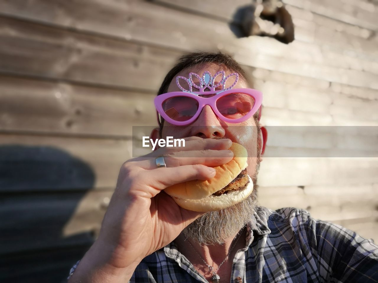 Portrait of man in novelty glasses eating burger against wall
