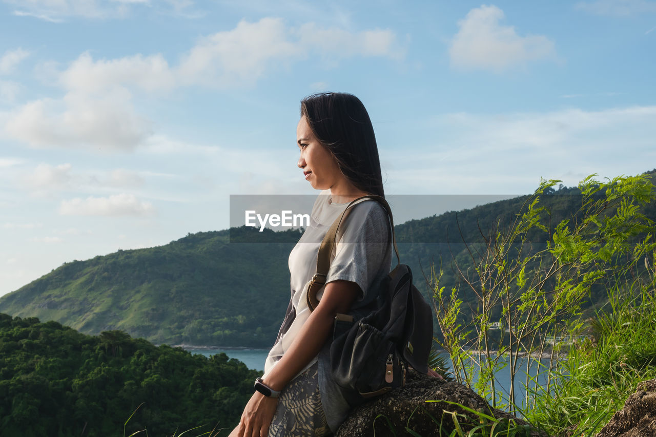 Side view of young woman looking at mountains against sky