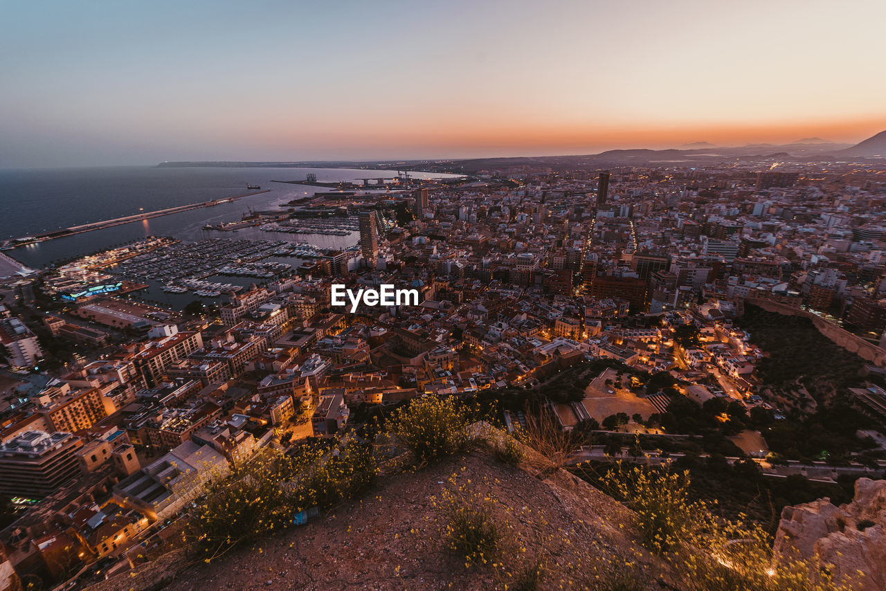 Aerial view of cityscape by sea against sky at sunset