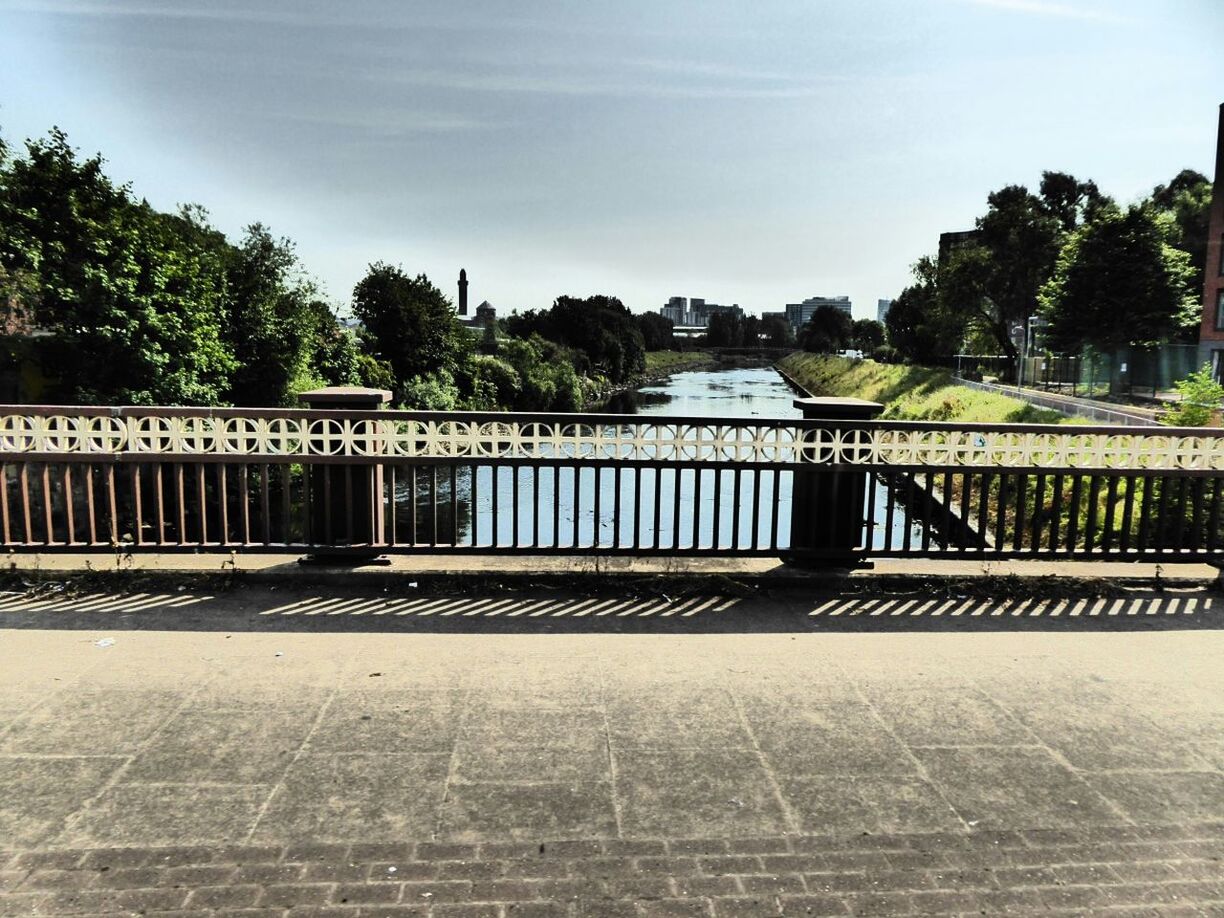 Railing amidst street and canal on sunny day