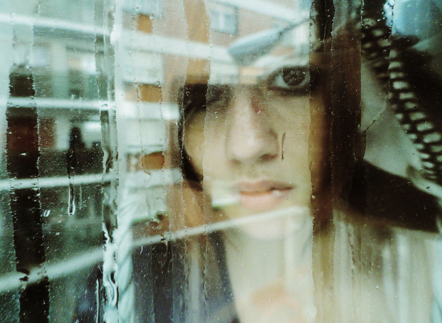 Reflection of young woman on wet glass window