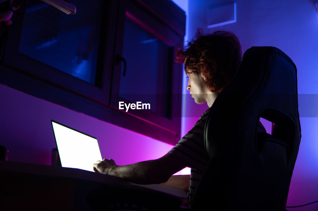 Man using laptop while sitting in darkroom