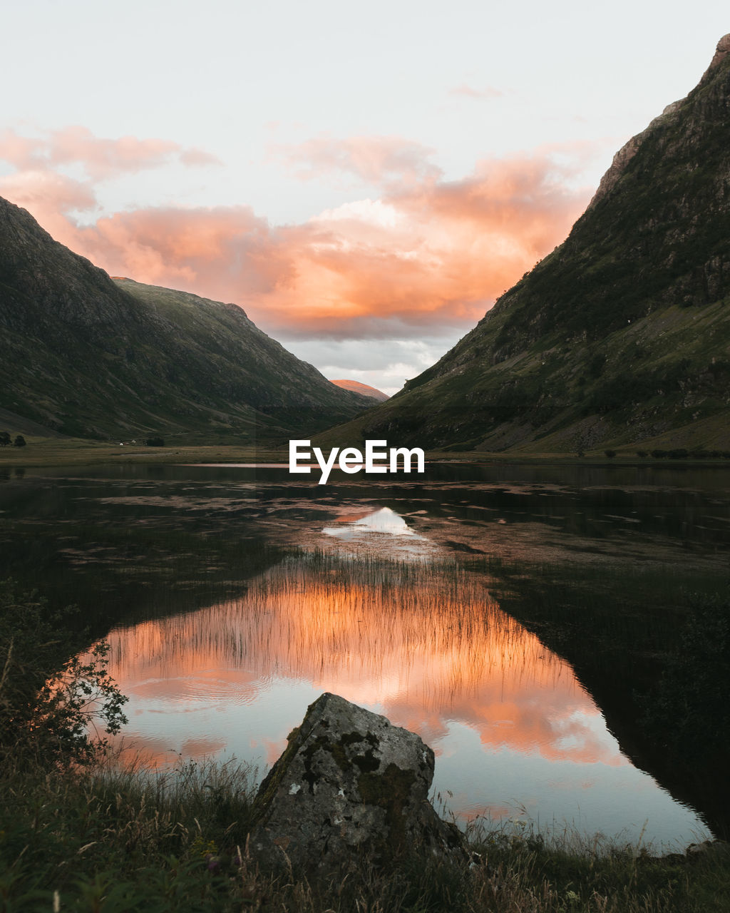 Scenic view of mountains and pink clouds reflected in lake 