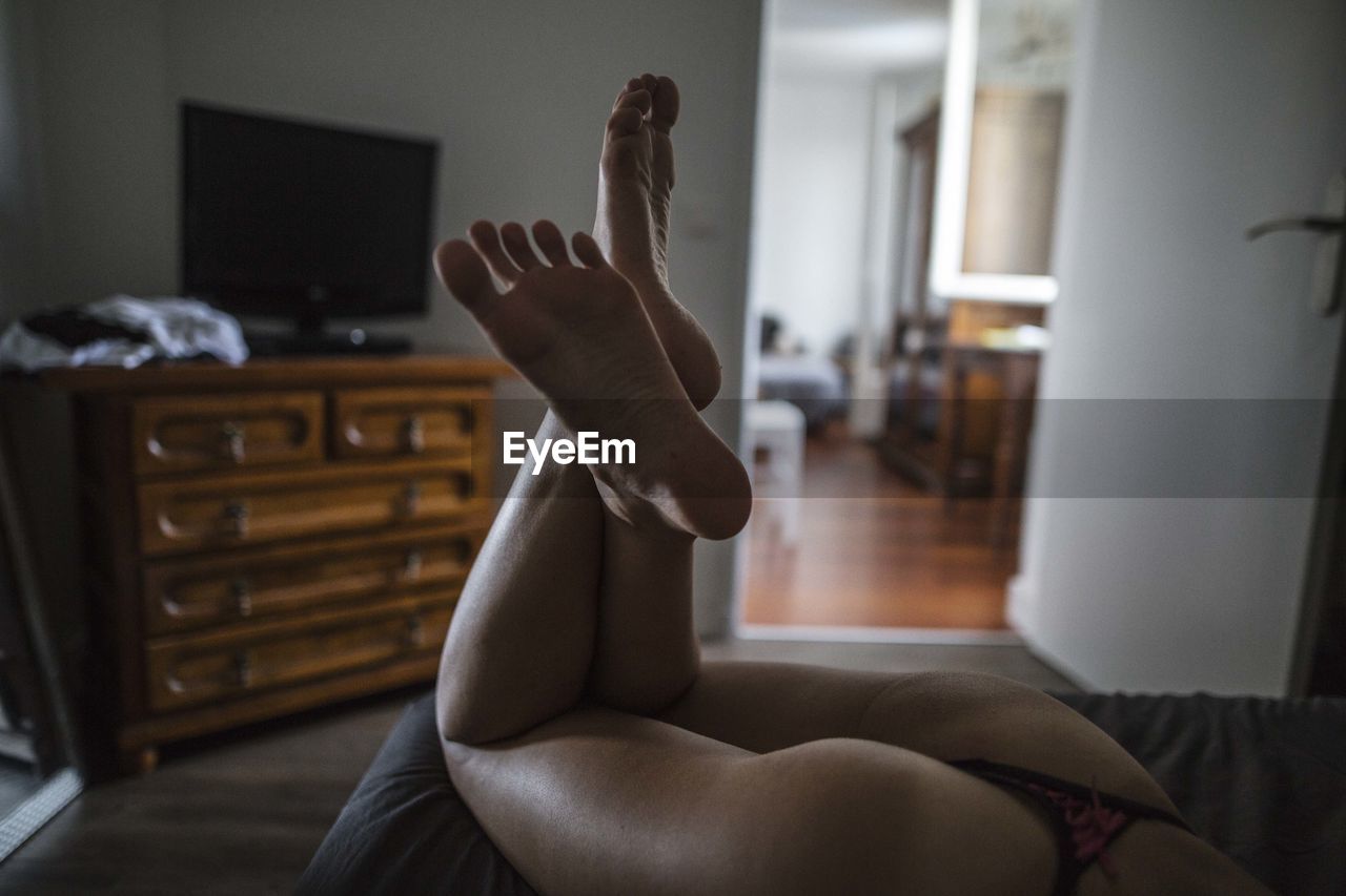 Low section of seductive woman lying on bed at home