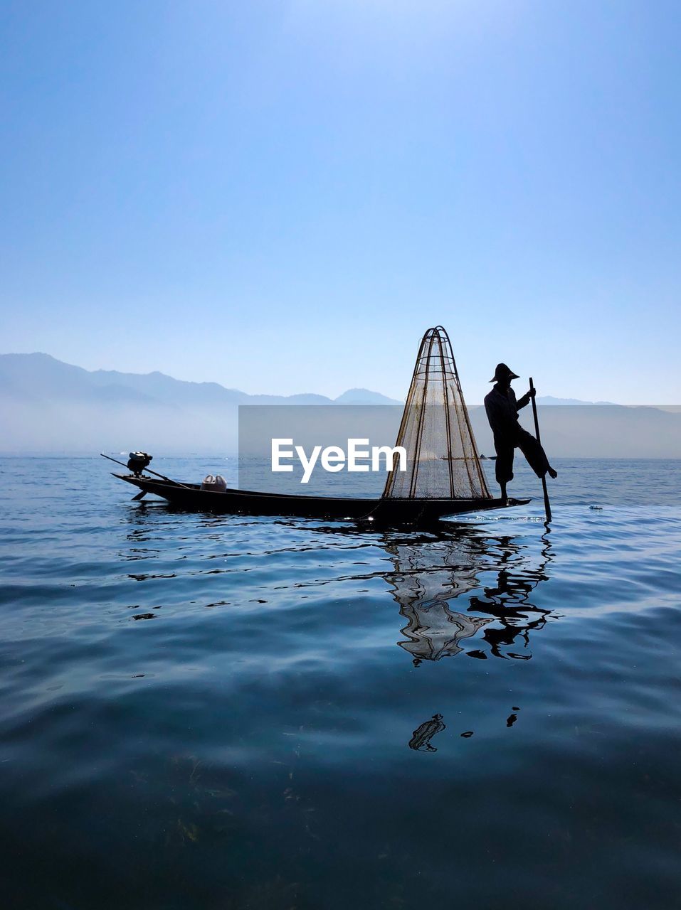 Fisherman on boat in lake against sky