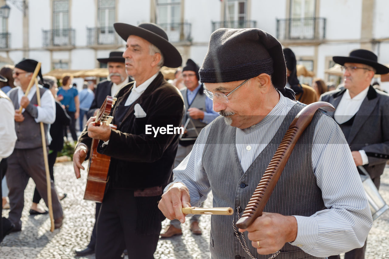 group of people, men, person, adult, architecture, city, day, arts culture and entertainment, music, hat, musical instrument, clothing, crowd, mature adult, musician, celebration, outdoors, street, event, standing, holding, tradition