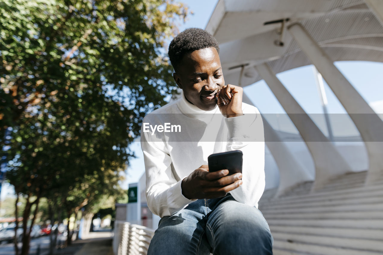 Smiling young man using mobile phone on railing