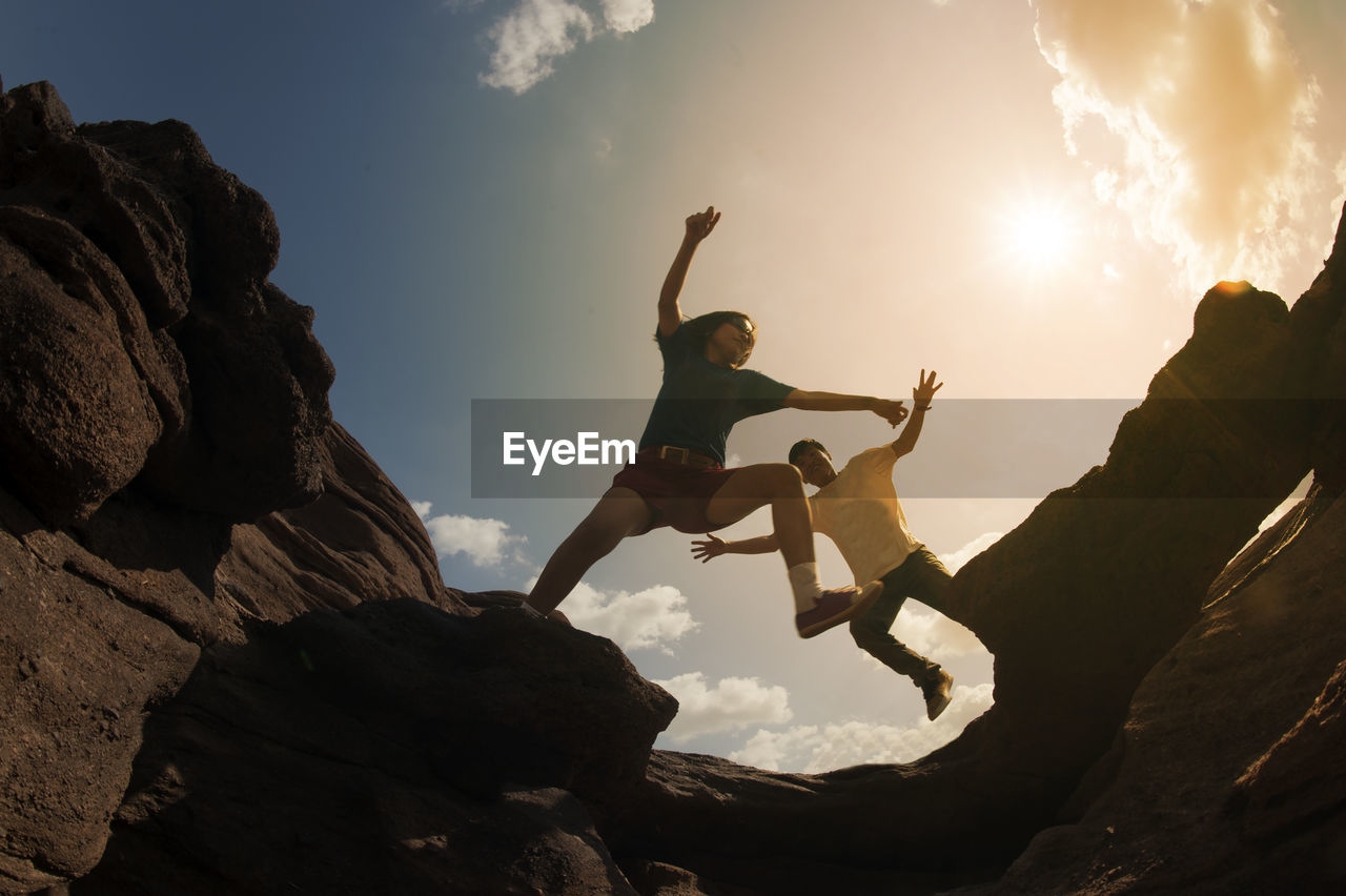 Low angle view of friends jumping over rock formations against sky