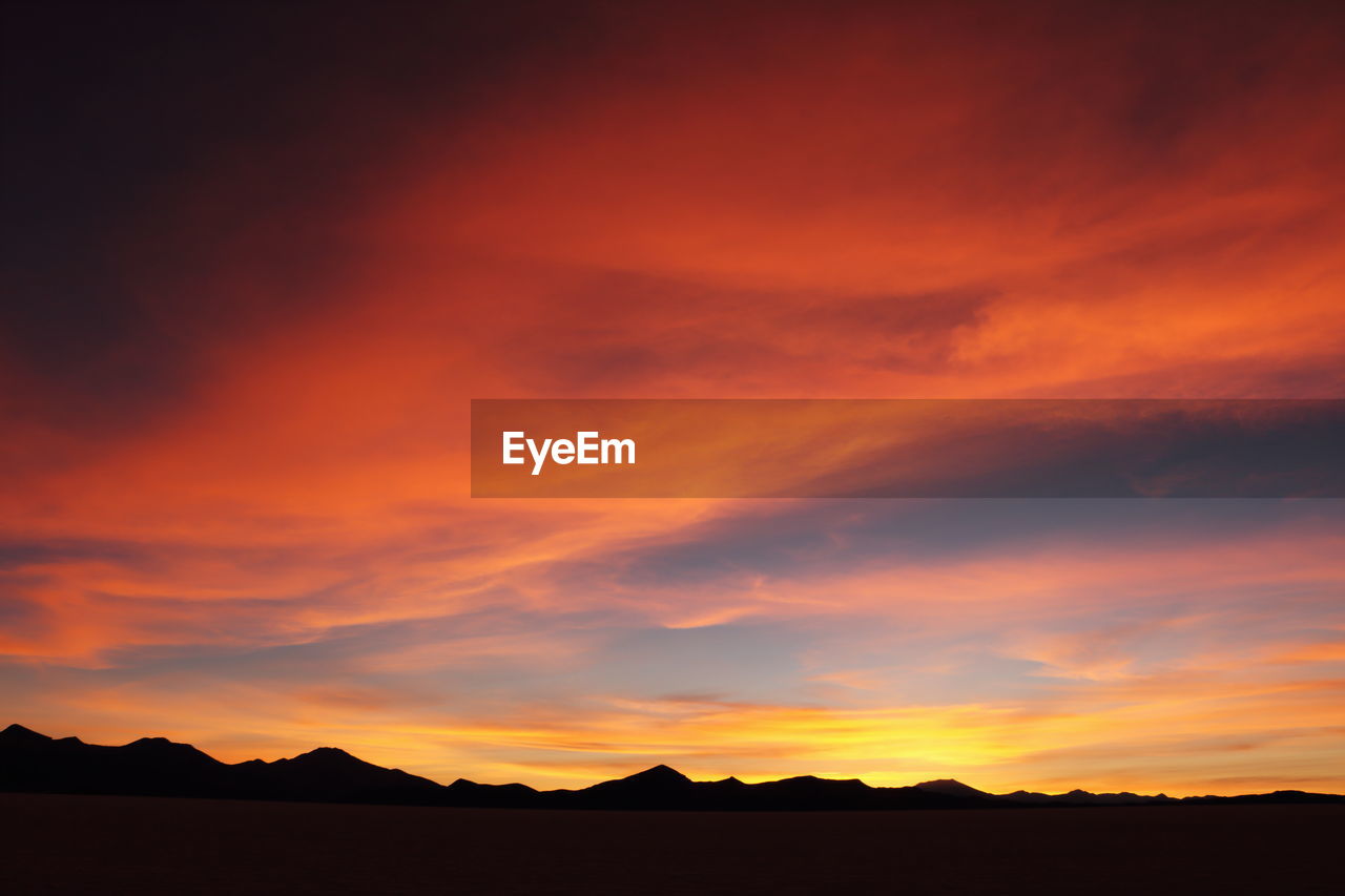 Silhouette landscape against dramatic sky during sunset