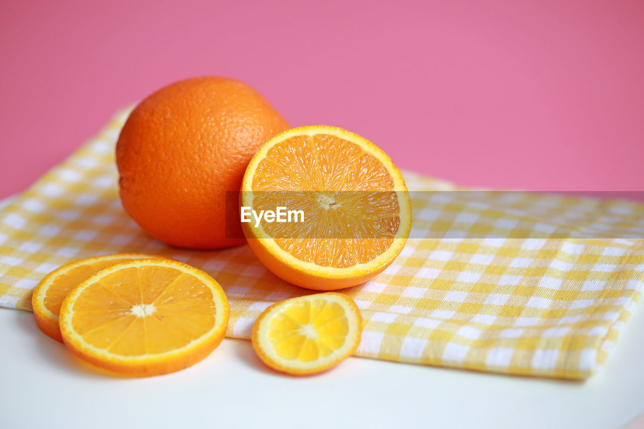 CLOSE-UP OF ORANGE FRUIT AGAINST COLORED BACKGROUND