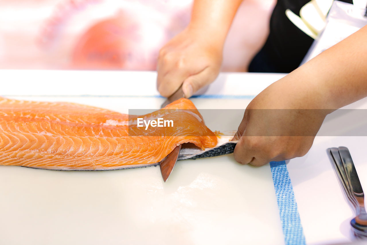 Cropped hands of chef cutting fish in commercial kitchen