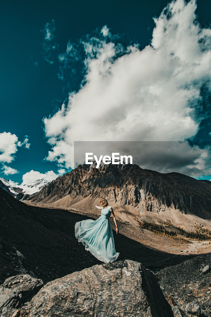 MAN ON ROCK AGAINST MOUNTAIN RANGE