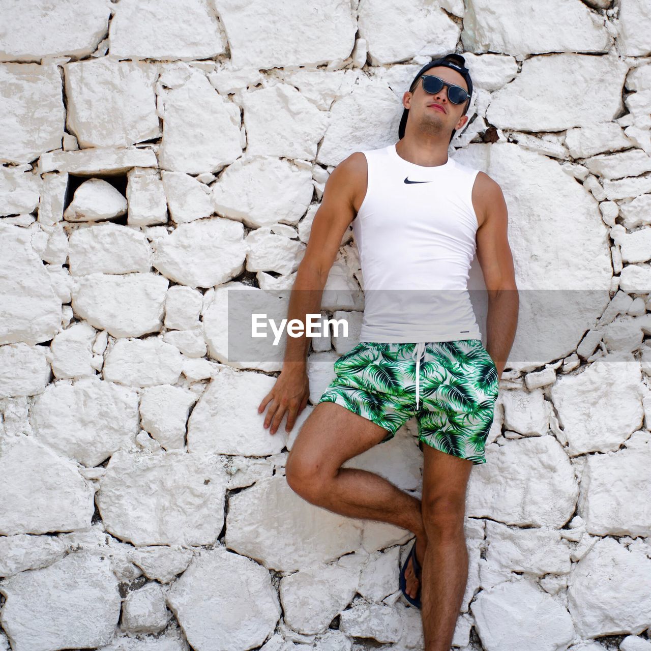 YOUNG WOMAN WEARING SUNGLASSES STANDING AGAINST WALL