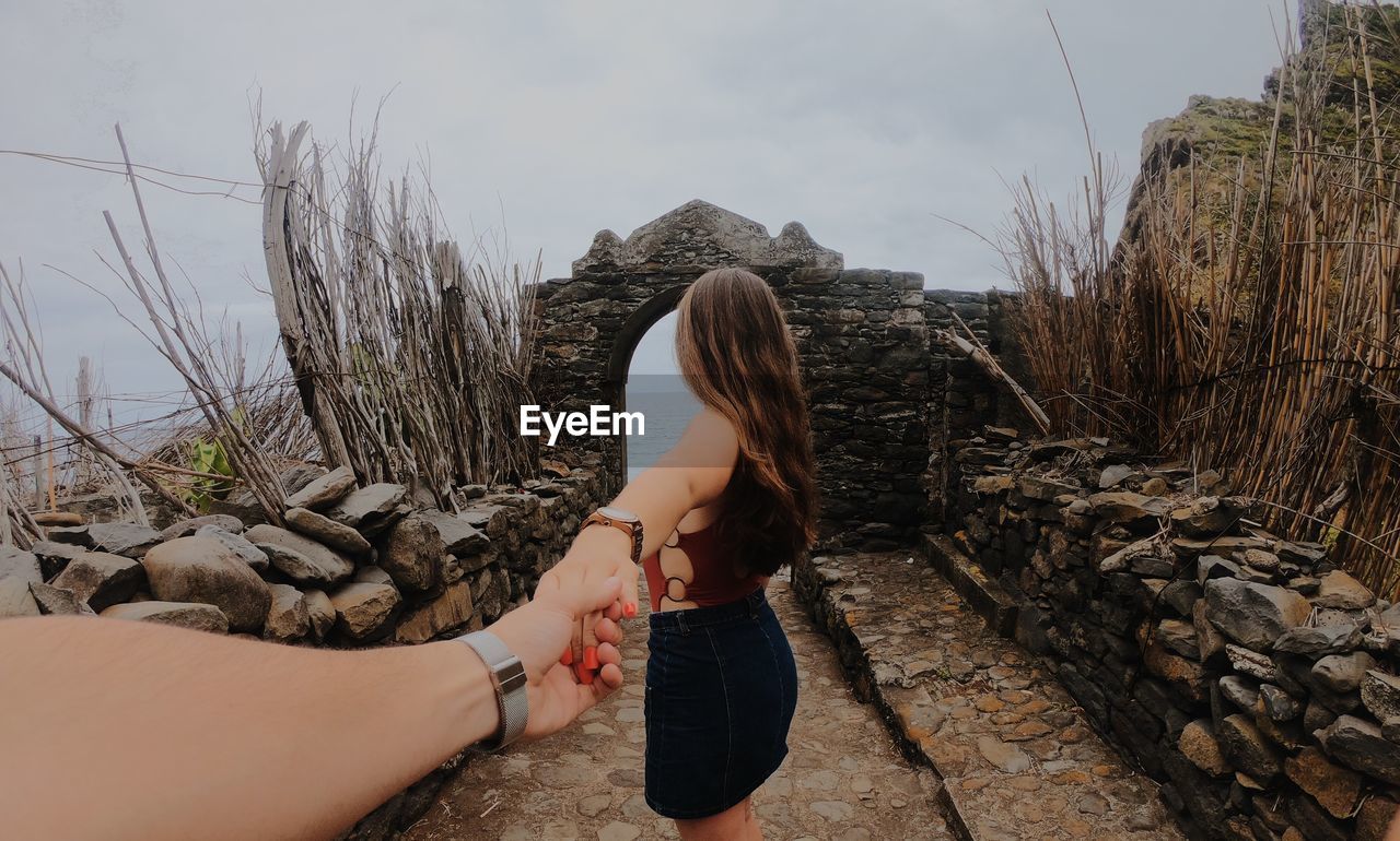 Cropped image of woman holding friend hands on fort against sky