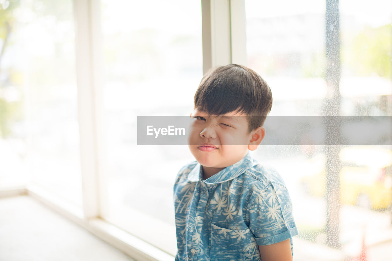 Portrait of cute boy sitting against window at home