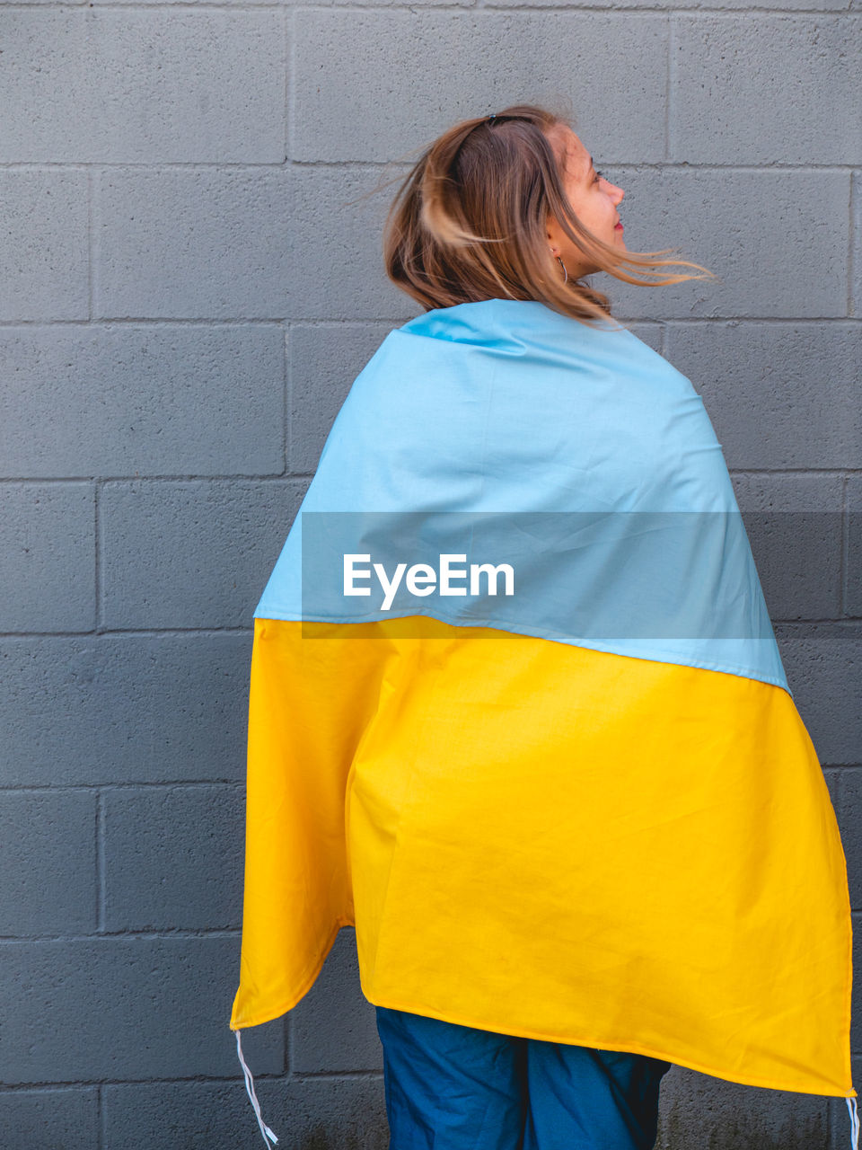 Caucasian blond teenager wrapped in an ukrainian flag over a neutral background 