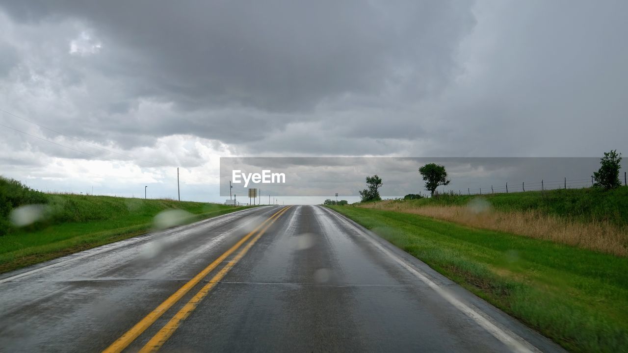 Road amidst grassy field against cloudy sky