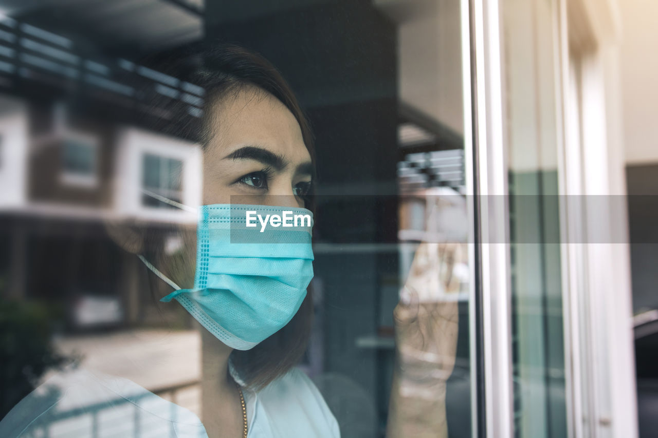 Close-up of woman wearing mask seen through window