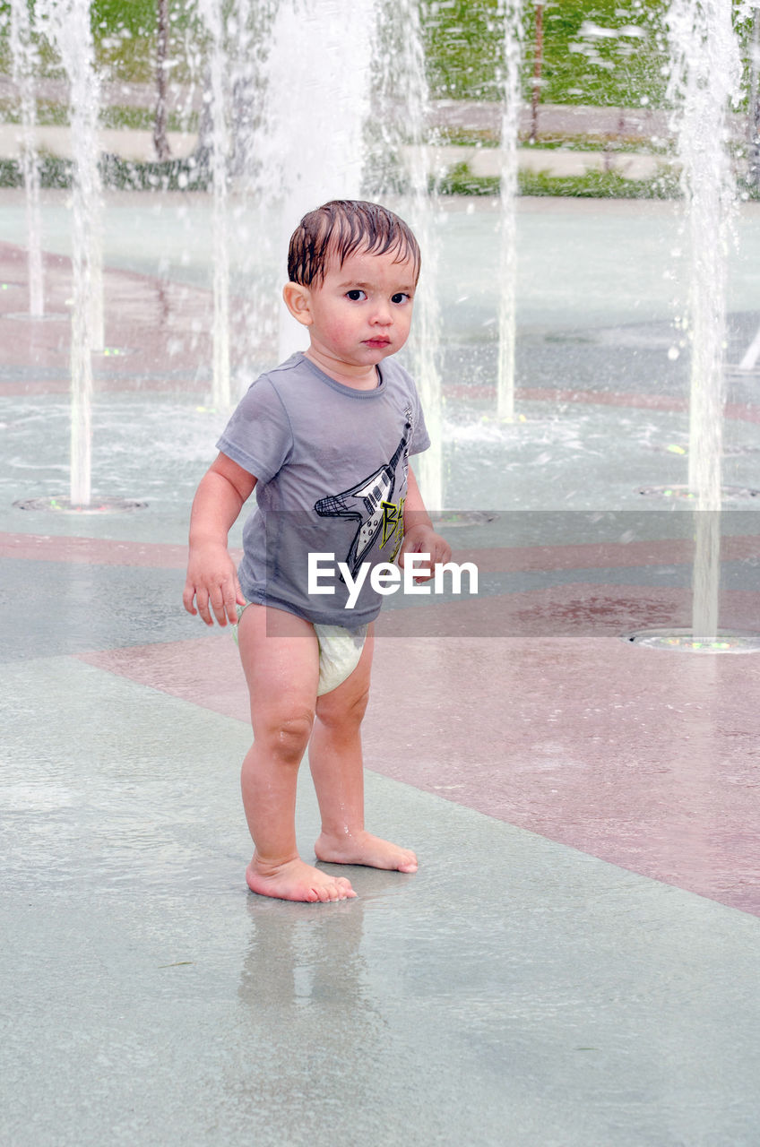 childhood, child, one person, full length, water, men, innocence, wet, motion, day, emotion, happiness, standing, nature, cute, toddler, fun, casual clothing, lifestyles, outdoors, enjoyment, spring, front view, smiling, splashing, person, portrait, fountain, baby, leisure activity, clothing, spraying, barefoot, looking, human face