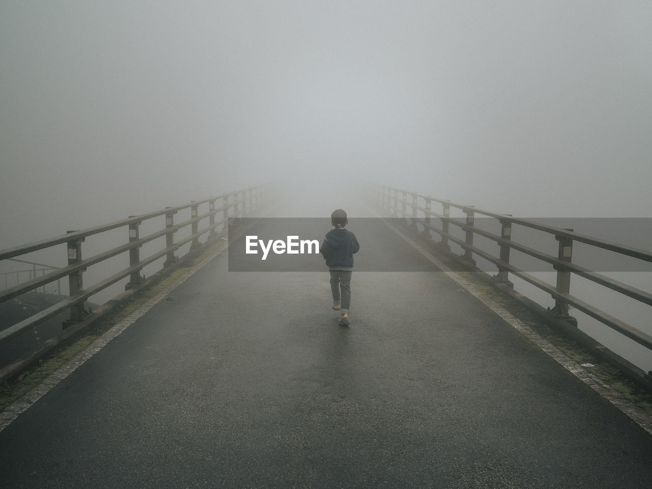 Rear view of boy walking on bridge during foggy weather