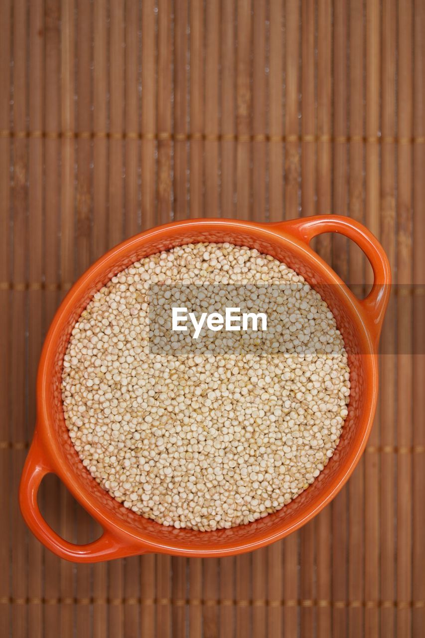 Raw quinoa in an orange bowl on a bambu mat