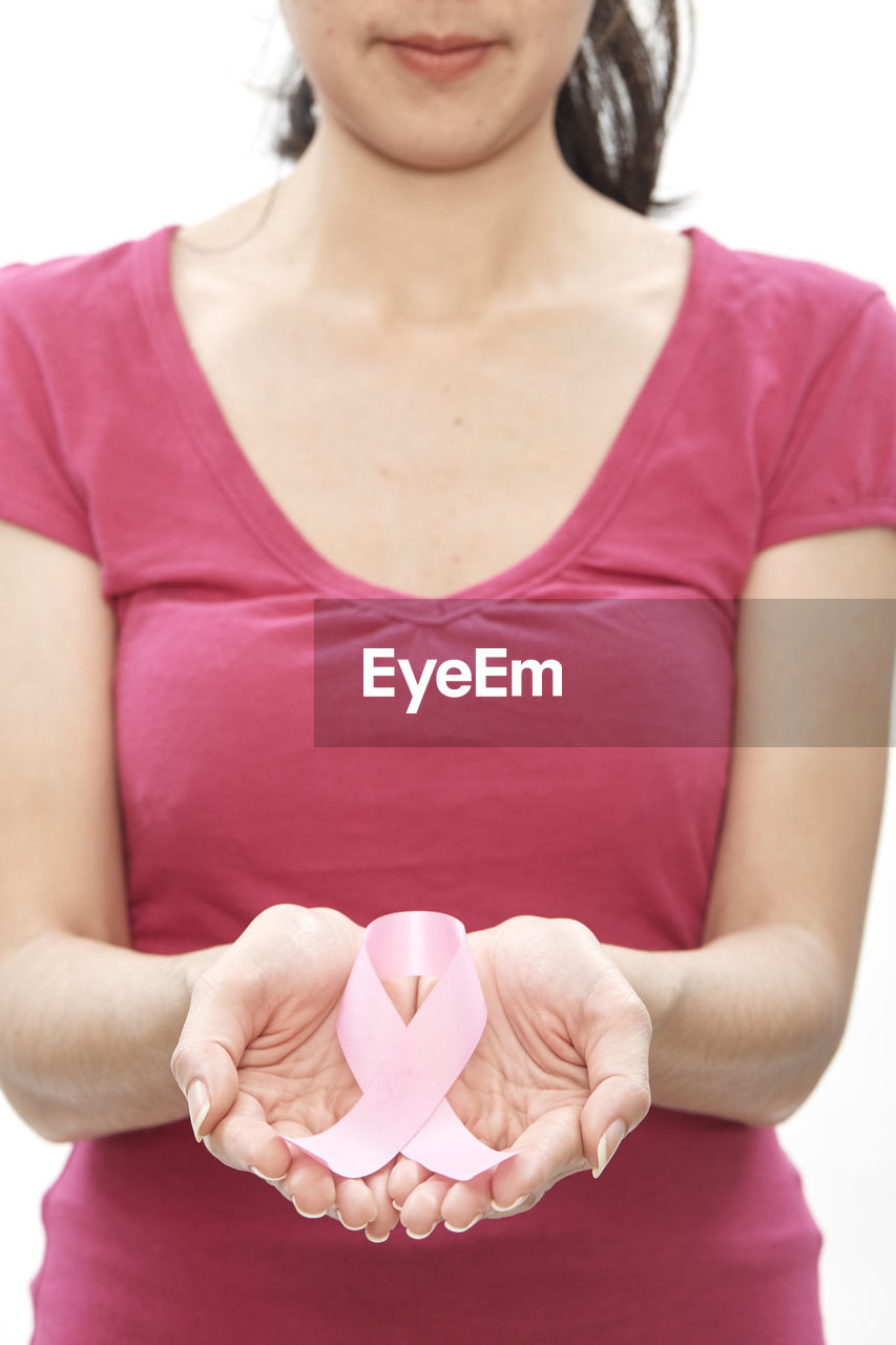 Midsection of woman holding breast cancer awareness ribbon against white background