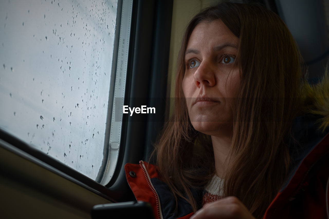 Young woman window transport. a thoughtful dark-haired girl looks out the window with raindrops