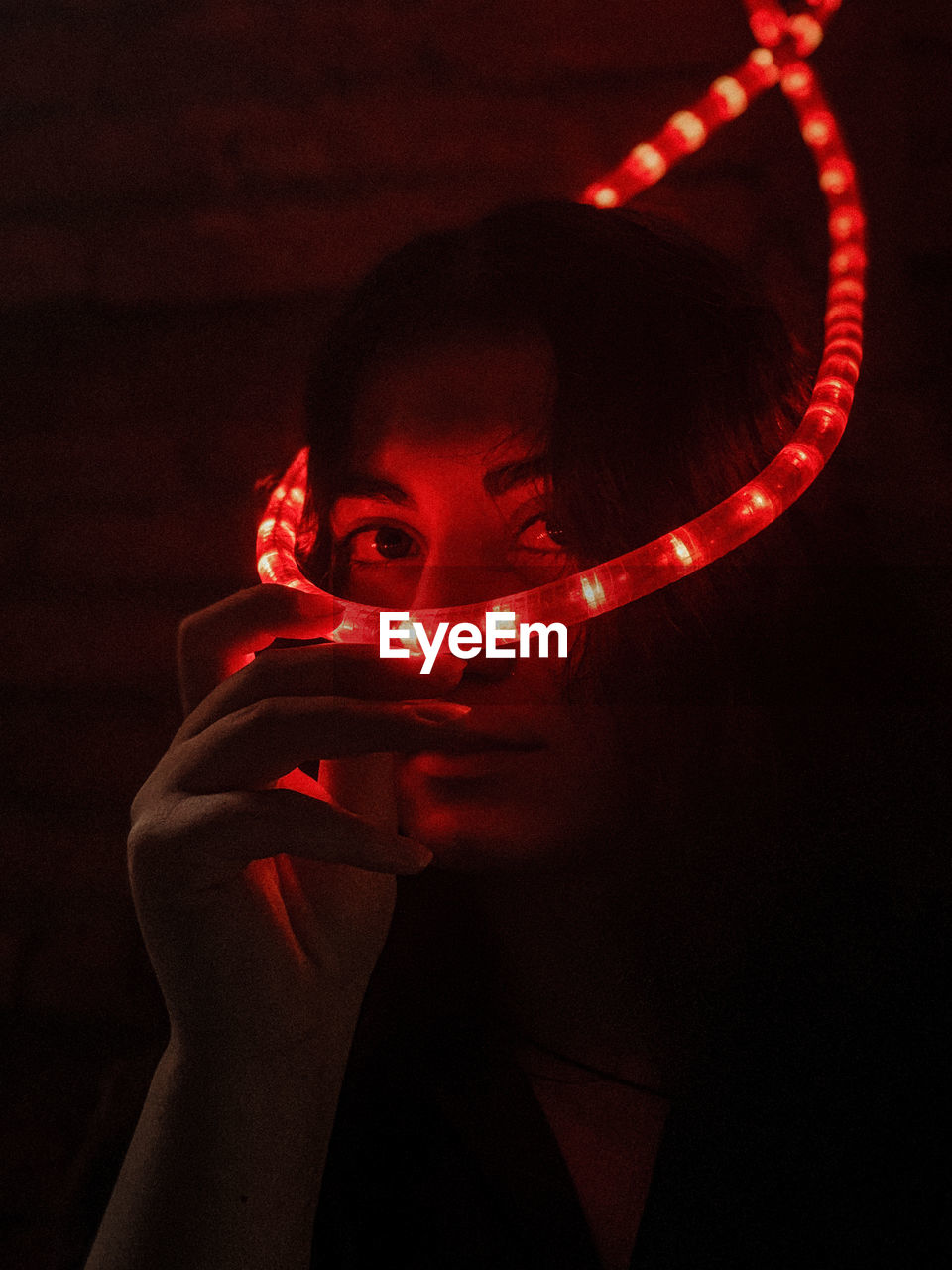 Portrait of woman holding illuminated lighting equipment in darkroom