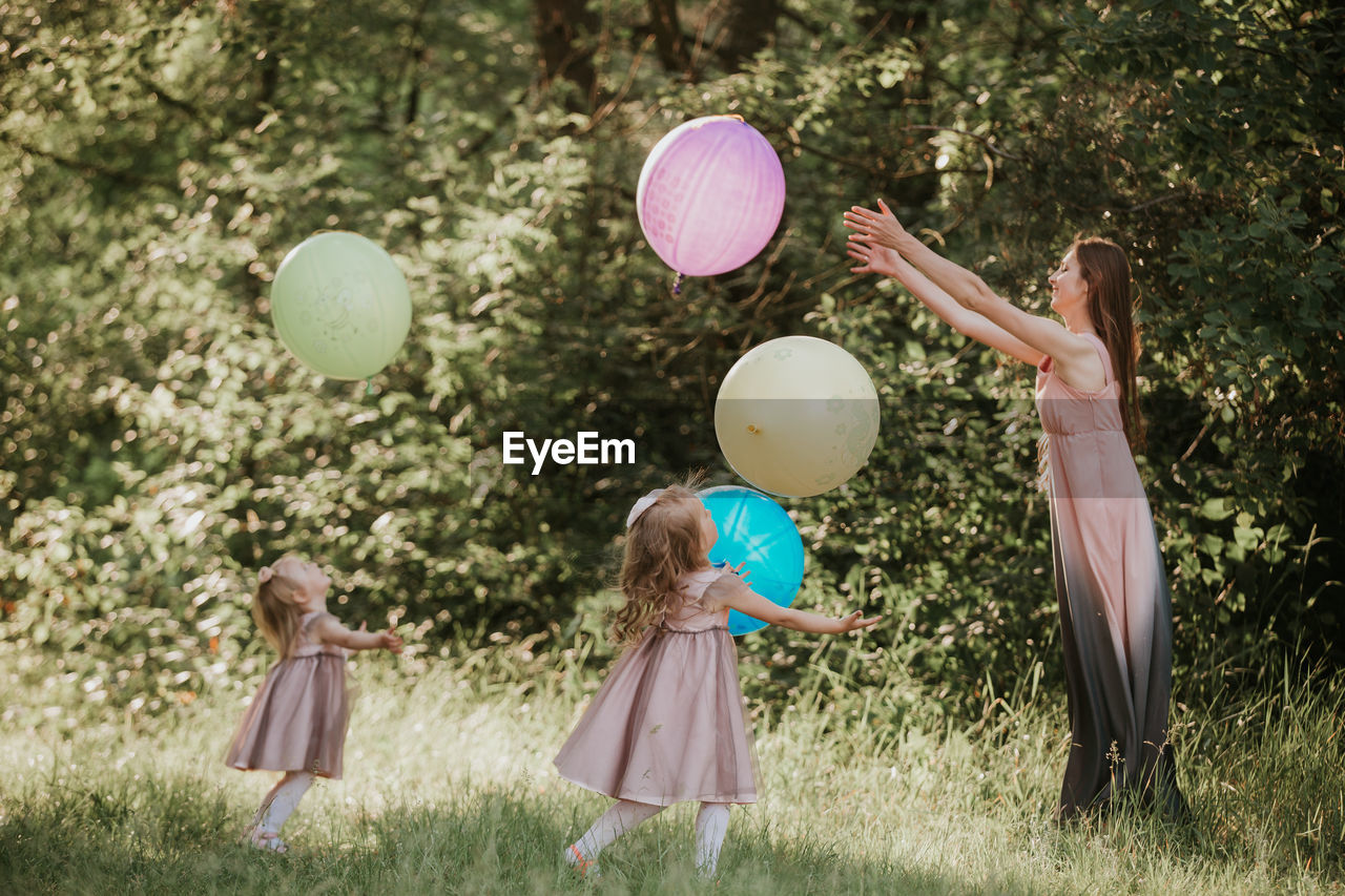 Mother and daughters playing with balloon against trees