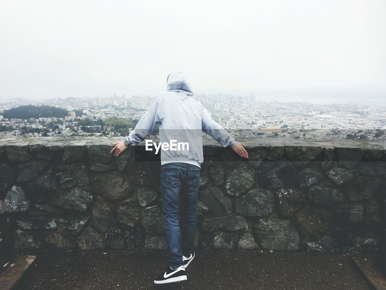 Rear view of man standing by retaining wall against clear sky