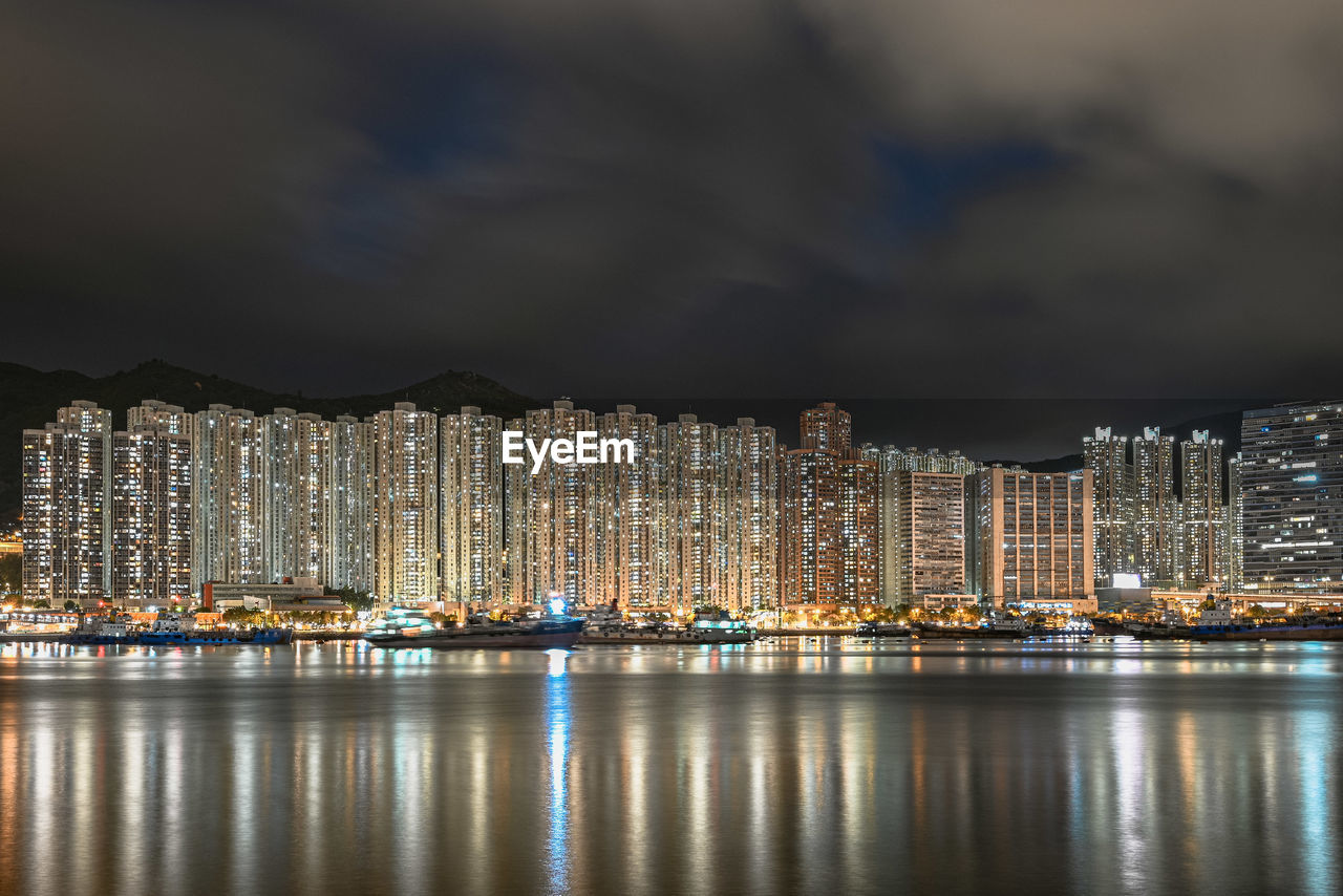 Illuminated city by sea against sky at night