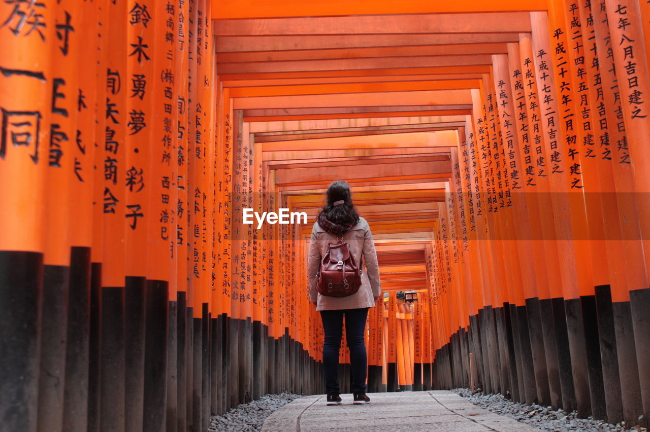 Rear view of woman standing amidst torii gates at fushimi inari shrine