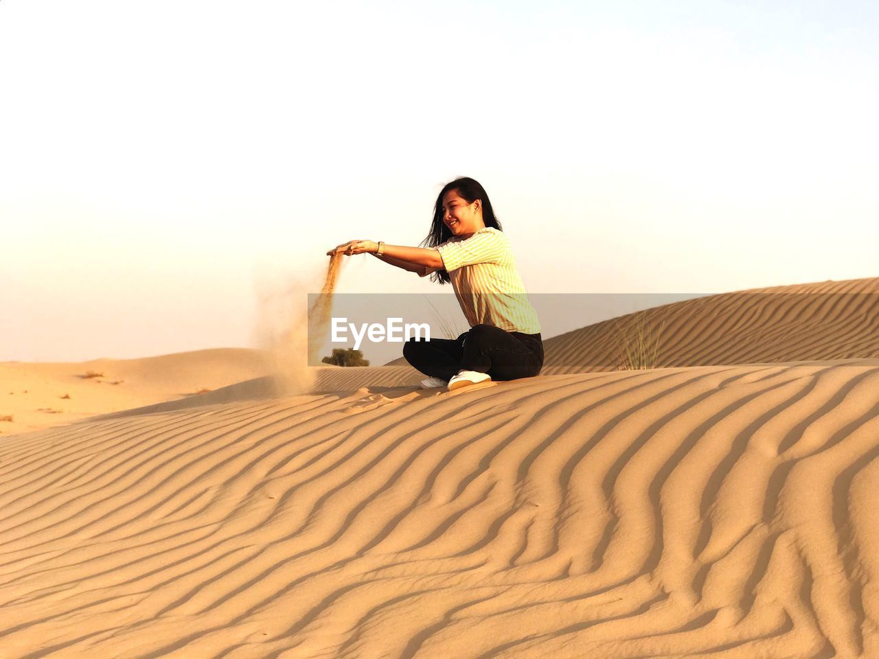 Woman playing with sand while sitting against sky