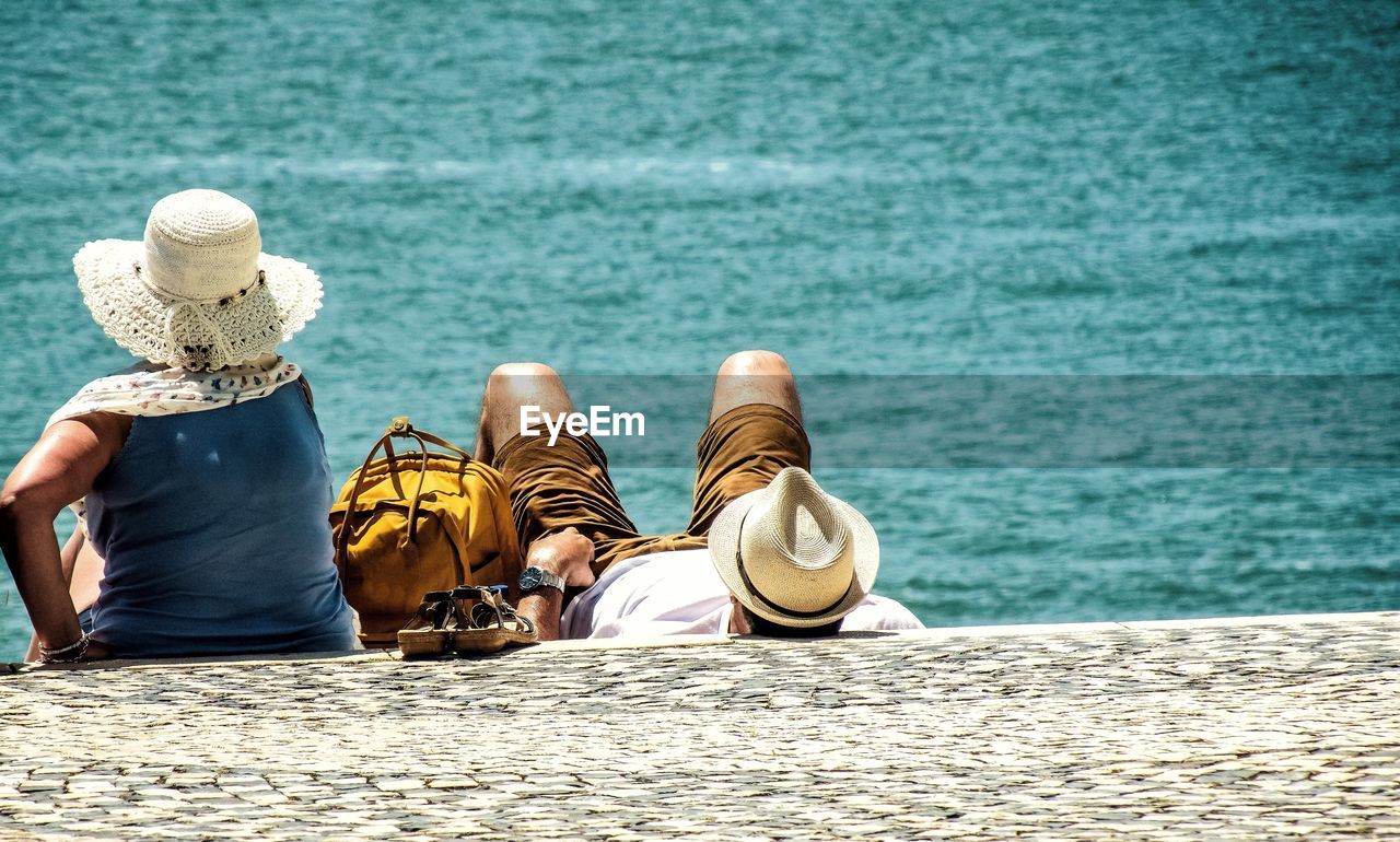 Rear view of couple relaxing at beach on sunny day