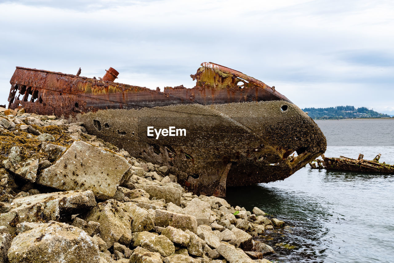 ABANDONED BOAT ON ROCK AGAINST SKY